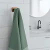 A green towel hanging on a wooden hook on a tiled wall in a bathroom. Anteprima dell’immagine prodotto