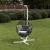 A hanging chair with cushions is placed on a grassy lawn in a garden setting, with bushes and a fence in the background. Podgląd zdjęcia produktu