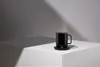 A black Ember mug sits on its charging coaster on a white surface, with dramatic lighting and shadows. Náhled obrázku produktu
