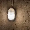 A close-up shot of a wall-mounted light fixture with a protective cage, set against a textured, rough wall. Produktbild-Vorschau