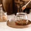 A honey jar with a dipper, on a wooden tray, with other jars in the background. Náhľad obrázku produktu