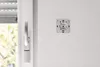 A close-up of a white wall with a white wall-mounted device and a white window handle and sensor. Produktbild-Vorschau
