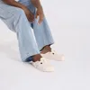 A person wearing light blue jeans and pink Birkenstock clogs, sitting against a white background. Podgląd zdjęcia produktu