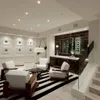 A modern living room with white chairs, a striped rug, and a wine cellar in the background. Náhled obrázku produktu