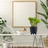 A modern dining area with white chairs, a white table, and a framed picture on a white paneled wall. A plant in a black pot sits on the table, with a bowl of fruit next to it. Náhľad obrázku produktu