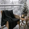 A cozy balcony scene in the snow with a chair, blanket, lantern, and a small Christmas tree. Produktbild-Vorschau