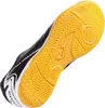 A single black and white indoor soccer shoe with a yellow sole is shown from a diagonal angle, highlighting the sole's tread pattern. Náhľad obrázku produktu