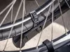 A close-up view of a bicycle wheel with a black strap attached to the tire and a black plastic component. Voir les images du produit