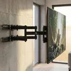 A black TV wall mount is attached to a concrete wall, holding a large TV displaying a nature scene. Náhľad obrázku produktu