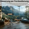A heater on a tripod in a modern living room with a large window overlooking a mountain landscape. Produktbild-Vorschau