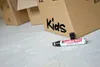 A permanent marker lies on a concrete floor next to cardboard boxes labeled 'Kids'. Produktbild-Vorschau
