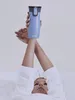 A person lying down, holding a blue Contigo travel mug above their head. Náhled obrázku produktu