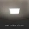 A square LED ceiling light is mounted on a ceiling, with text below. Produktbild-Vorschau