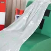 A soft blanket with a Minecraft Creeper pattern is draped over a green chair. A red and orange striped pillow is visible behind the blanket. Podgląd zdjęcia produktu