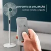 A hand holding a remote control for a fan, with the fan in the background. Voir les images du produit