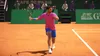 A tennis player in mid-swing on a clay court, with spectators and advertising in the background. Produktbild-Vorschau