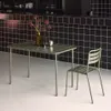 A khaki-colored metal table and chair set against a black tiled wall. Produktbild-Vorschau