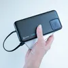 A hand holds a black power bank charging a white smartphone. Anteprima dell’immagine prodotto