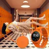 A woman is floating in a school hallway with lockers, and a smartwatch and its case are in the foreground. Voir les images du produit