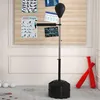 A boxing stand with a punching bag and reflex bar is set up in a room with a bulletin board on the wall and weights on the floor. Produktbild-Vorschau