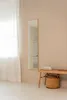 A minimalist interior scene with a full-length mirror and a wooden bench with a basket. Náhled obrázku produktu