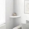 A white corner shelf with decorative items on it, in a room with a window and blinds. Produktbild-Vorschau