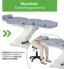 A medical or cosmetic treatment table with a person sitting on a stool next to it. Produktbild-Vorschau