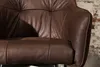 A close-up view of a brown leather armchair, showing the texture and stitching. Produktbild-Vorschau