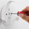A hand is using a screwdriver to attach a white wall mount to a textured wall. Náhled obrázku produktu