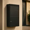 A black mailbox with a parcel compartment is mounted on a beige wall next to a dark gray door. Produktbild-Vorschau