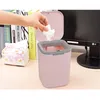 A hand is shown dropping a tissue into a small pink trash can on a desk, next to a stack of books and a box of tissues. Produktbild-Vorschau