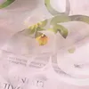 A close-up view of a sheer pink fabric with a floral pattern, layered over text. Produktbild-Vorschau