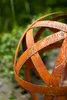 A close-up of a rusty metal sphere in a garden setting. Produktbild-Vorschau