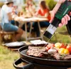 A group of people are having a barbecue outdoors, with one person using an electric salt and pepper grinder over a grill with steaks and vegetables. Produktbild-Vorschau