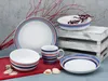 A set of ceramic dishes with blue and red stripes, arranged on a table with some decorative branches and seashells. Náhľad obrázku produktu