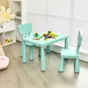 A child's table and chairs set with toys on the table, placed near a window with blinds. Produktbild-Vorschau