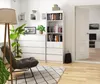 A modern living room with a white bookshelf, chest of drawers, and a chair. Produktbild-Vorschau