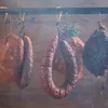 Several types of smoked meats and sausages are hanging from hooks in a smoking chamber. Produktbild-Vorschau