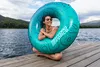 A woman sits on a wooden dock next to a lake, holding a large inflatable tube. Anteprima dell’immagine prodotto