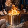 People gathered around a stainless steel fire pit with a roaring fire. Produktbild-Vorschau