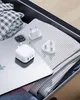 A travel charger and adapters are placed inside an open suitcase with folded clothes. Produktbild-Vorschau