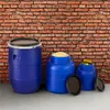 Three blue plastic barrels of different sizes are placed on a concrete floor in front of a brick wall. The largest barrel is on the left, and the two smaller ones are to its right. The middle barrel is filled with a light-colored granular substance, and th Produktbild-Vorschau