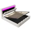 A beige upholstered bed frame with its mattress support lifted, revealing storage space underneath. The headboard features integrated pink LED lighting. Náhled obrázku produktu