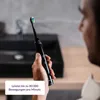 A person is holding a black electric toothbrush in a bathroom setting. Produktbild-Vorschau