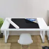 A puzzle mat is laid out on a white table, partially covered by a black mat, with a rolled-up tube next to it. A white chair is in front of the table. Anteprima dell’immagine prodotto