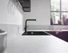 A modern kitchen sink with a black faucet and a stream of water running into it, set against a light gray countertop and white wall. Anteprima dell’immagine prodotto