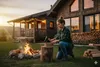 A woman chopping wood in front of a cabin with a campfire burning. Anteprima dell’immagine prodotto