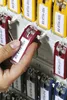 A hand is shown selecting a red key tag from a rack of key tags. Produktbild-Vorschau