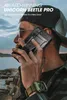A man wearing a cap and plaid shirt is holding a smartphone with a black case to his ear, with a body of water and rocky shore in the background. Náhled obrázku produktu