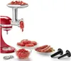 A red KitchenAid stand mixer attachment with a meat grinder, filled with meat, is shown. Ground meat, patties, and sausages are displayed in bowls and on plates, with sausage stuffing tubes to the side. Náhled obrázku produktu